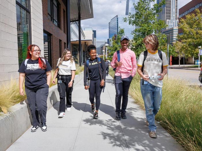 Five CU Denver students walking on sidewalk while talking to one another