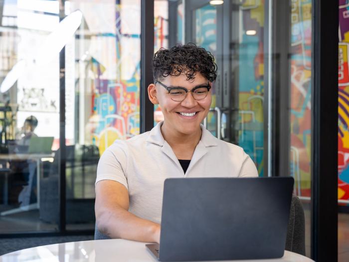 CU Denver student in a study room looking at laptop smiling