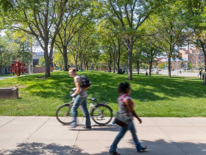 Landscape shot showing campus green area and pedestrians on sidewalk