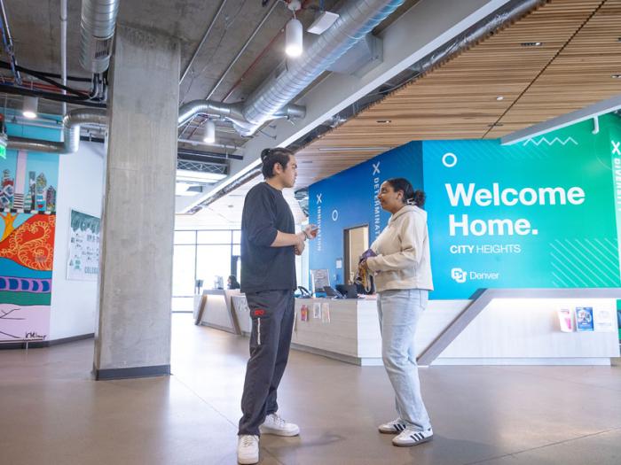 Two people talking in City Heights lobby with large sign in background that reads, "Welcome Home"