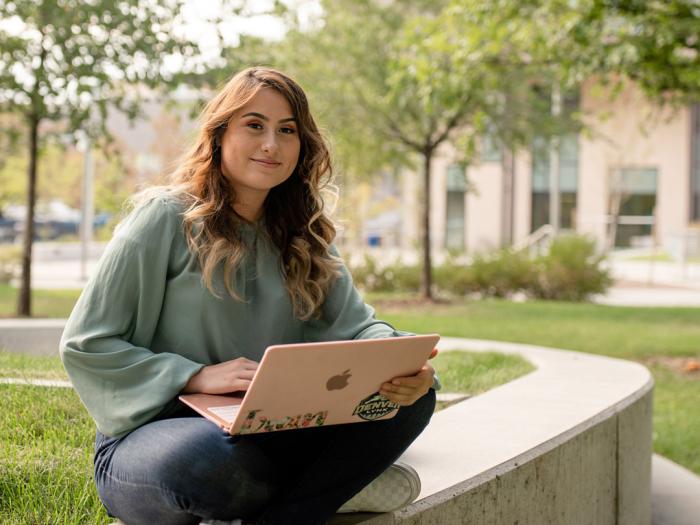 CU Denver student sitting on short wall while working on a laptop