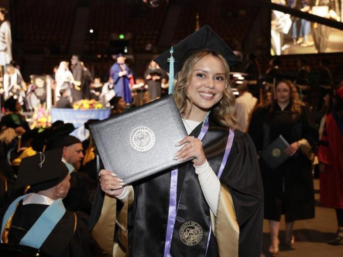 CU Denver graduate at Commencement holding diploma cover