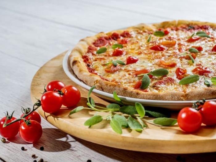 Pizza in a pan with tomatoes and basil leaves around the pizza
