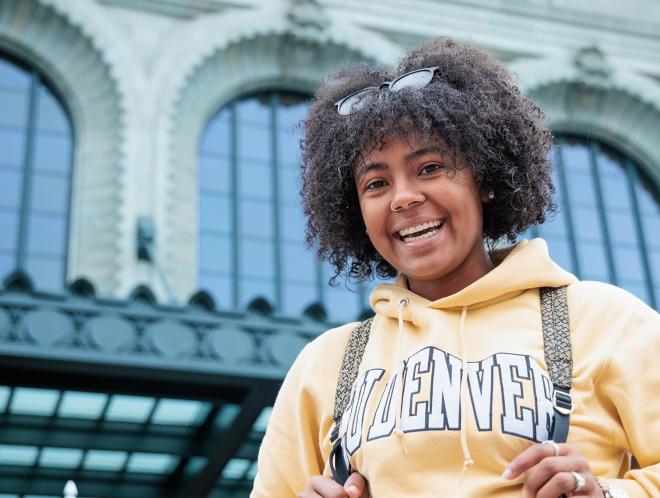 CU Denver student smiling down at building wearing a CU Denver gold hoodie