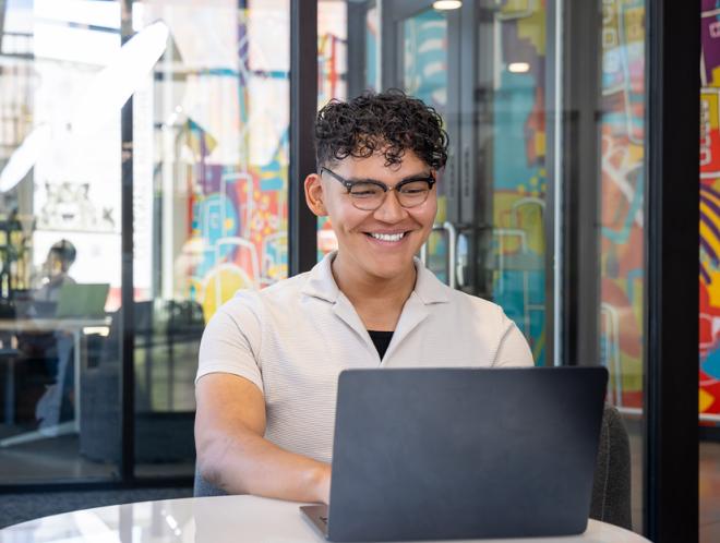 CU Denver student in a study room looking at laptop smiling