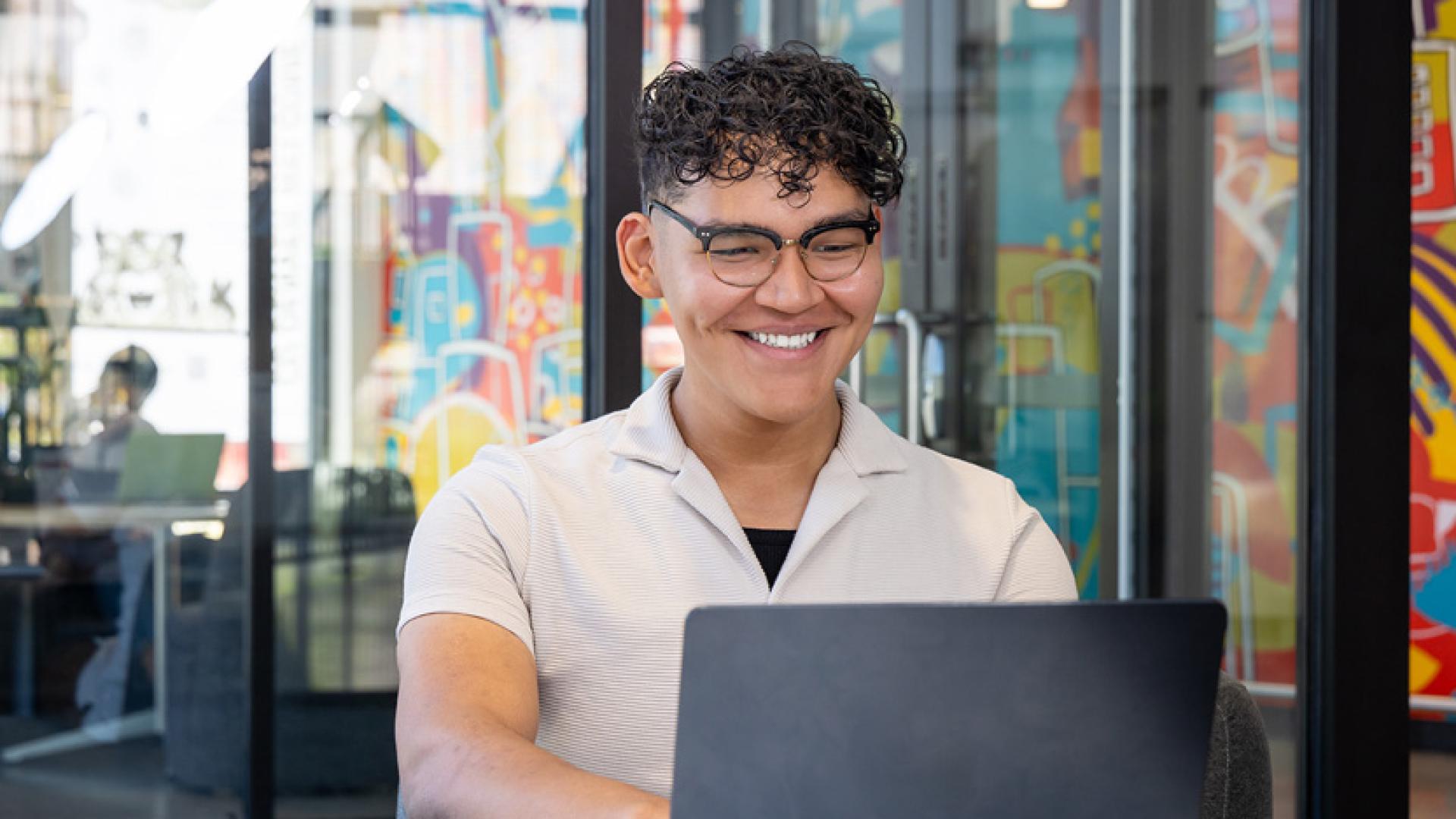 CU Denver student in a study room looking at laptop smiling