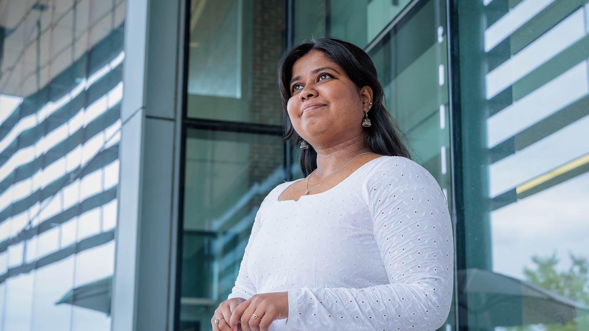 Student standing in front of windows of building looking off in the distance
