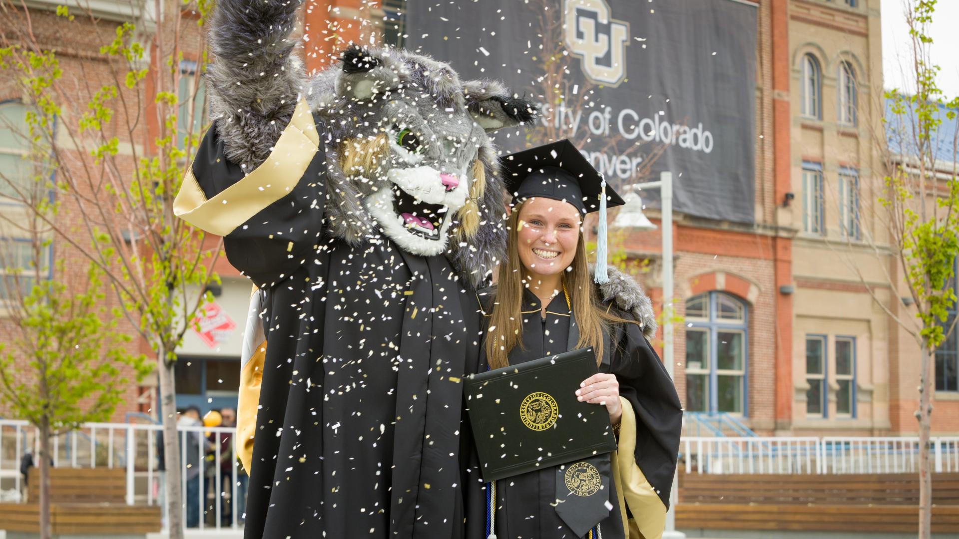Milo the mascot with a graduate student and confetti