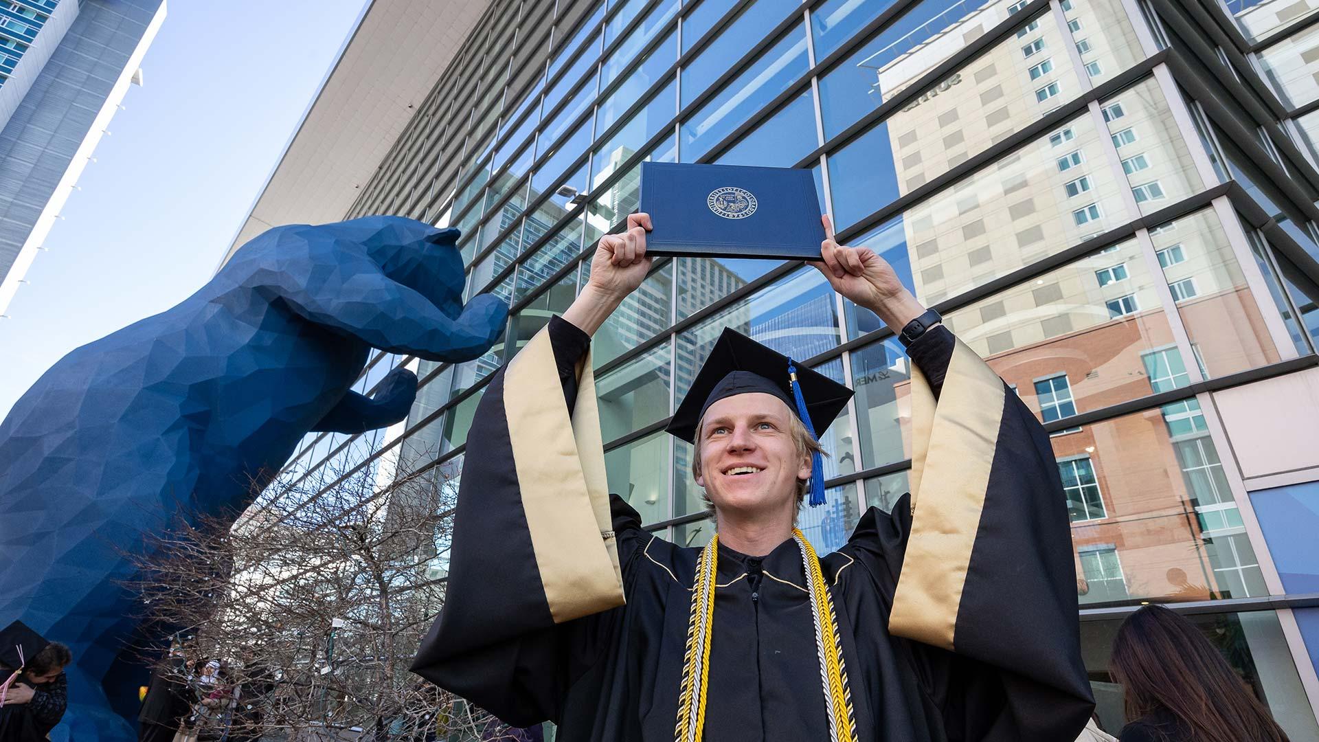 Graduate in regalia holding up diploma cover at commencement