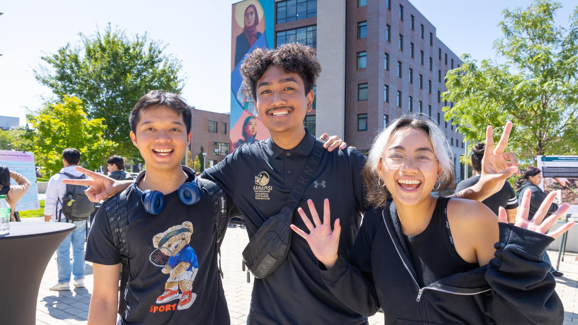 Three CU Denver students smiling and waving for camera