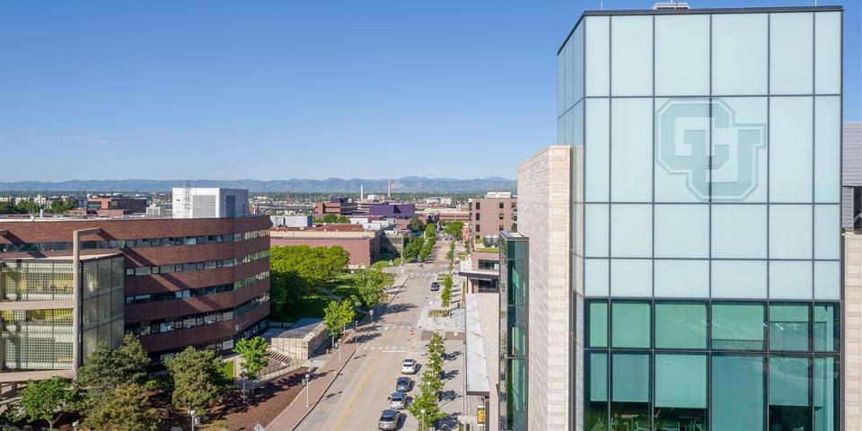 Aerial shot of CU Denver campus with a close up on the CU Logo etched into a building window with Rocky Mountains visible on the horizon in the background