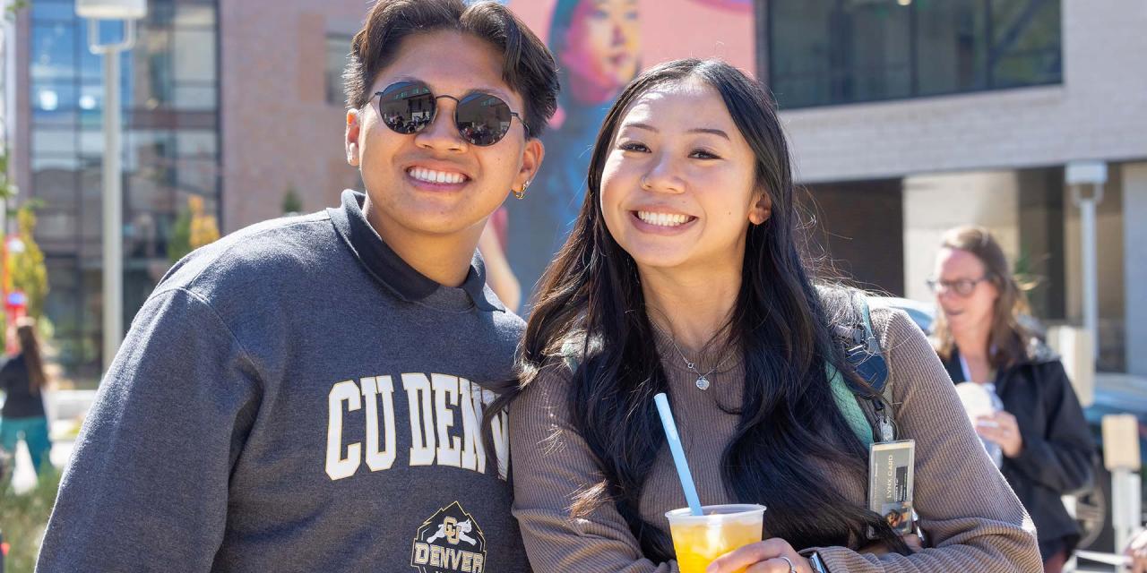 Two CU Denver students posing for picture outside while one is wearing a CU Denver hoodie and the other is holding a cup with boba tea