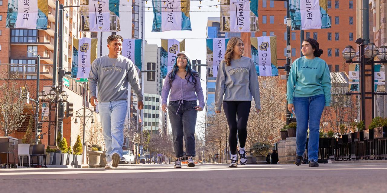 Four CU Denver students walking in Larimer Square with CU Denver flags