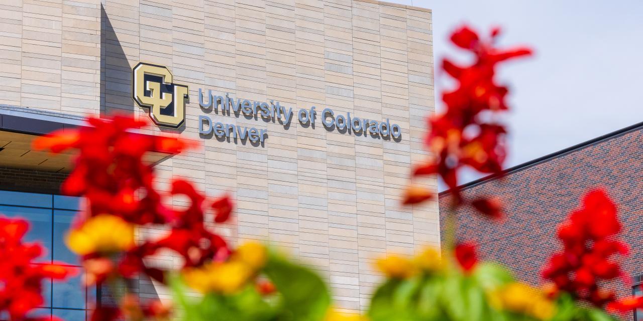 CU Denver building with the CU Denver logo showing with flowers in the foreground.