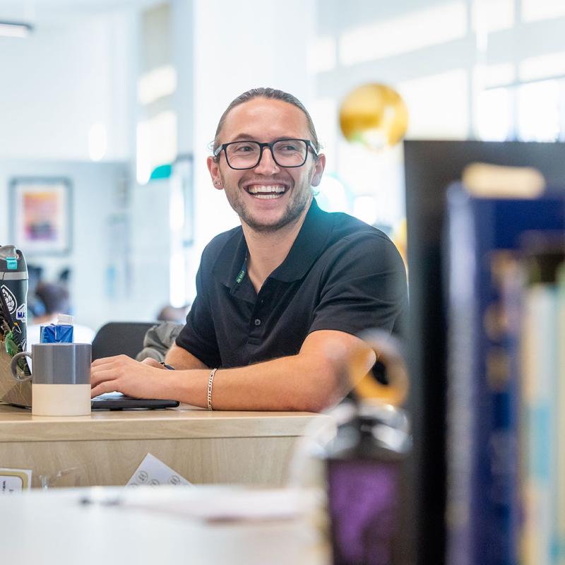 CU Denver student sitting at desk smiling and looking away from camera