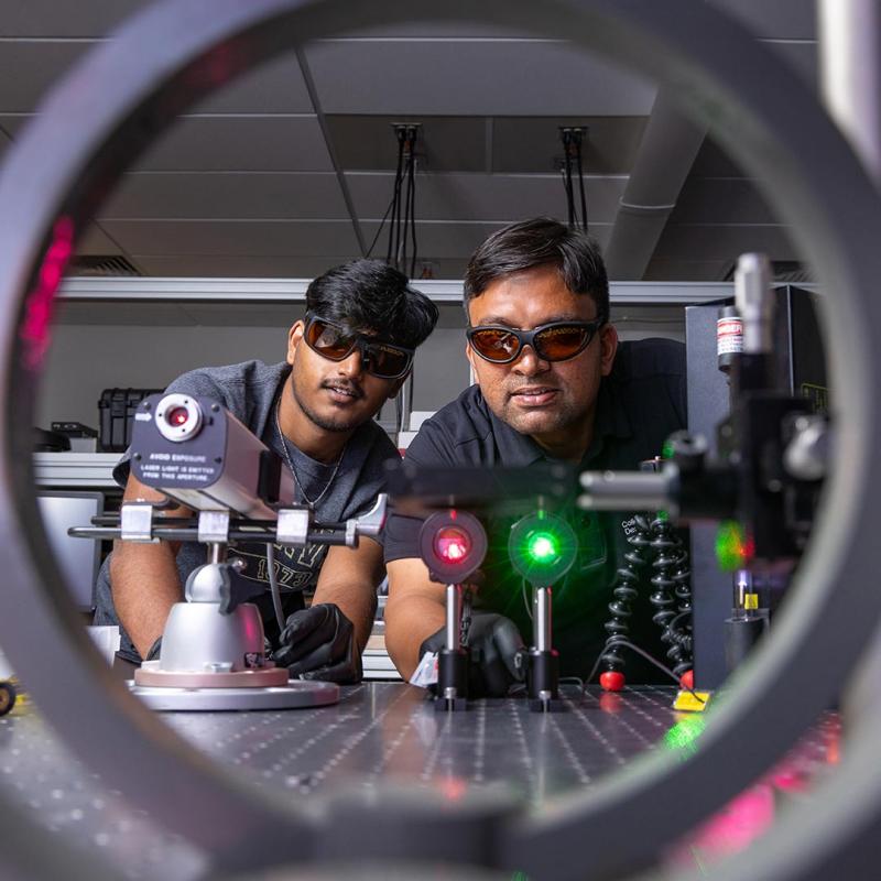 Two College of Engineering, Design, and Computing students working with lasers in lab