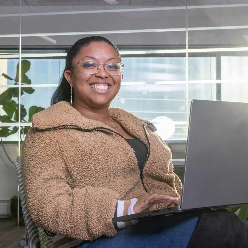 Student sitting outside working on open laptop and smiling at the camera