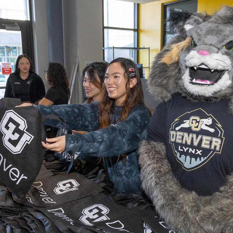 Students handing out CU Denver bags while standing by Milo the Lynx