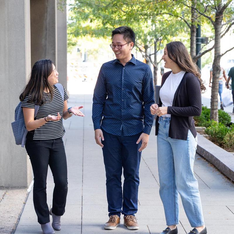 Three people dressed in business casual standing on sidewalk talking