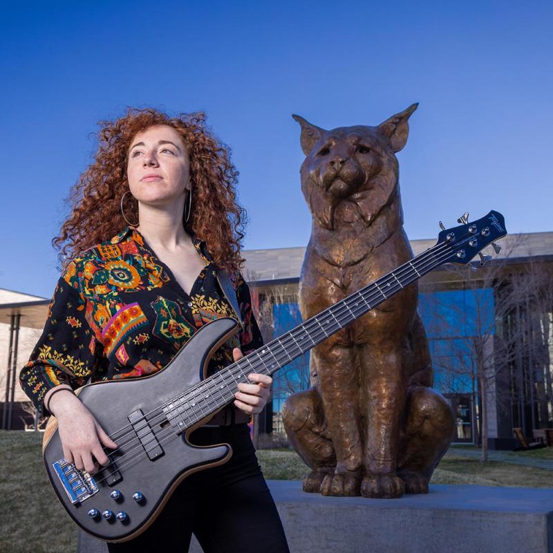 CU Denver alum, Zoe Moff, posing with guitar and Milo the Lynx Statue 