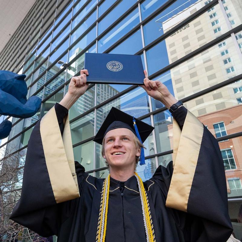 Graduate in regalia holding up diploma cover at commencement