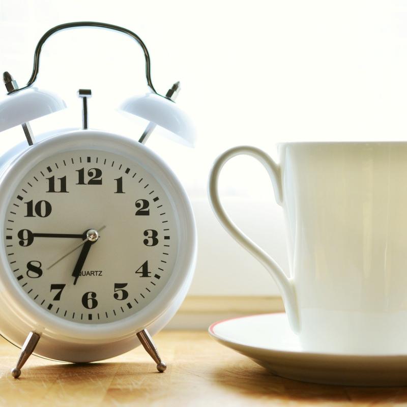 An alarm clock next to a cup of coffee